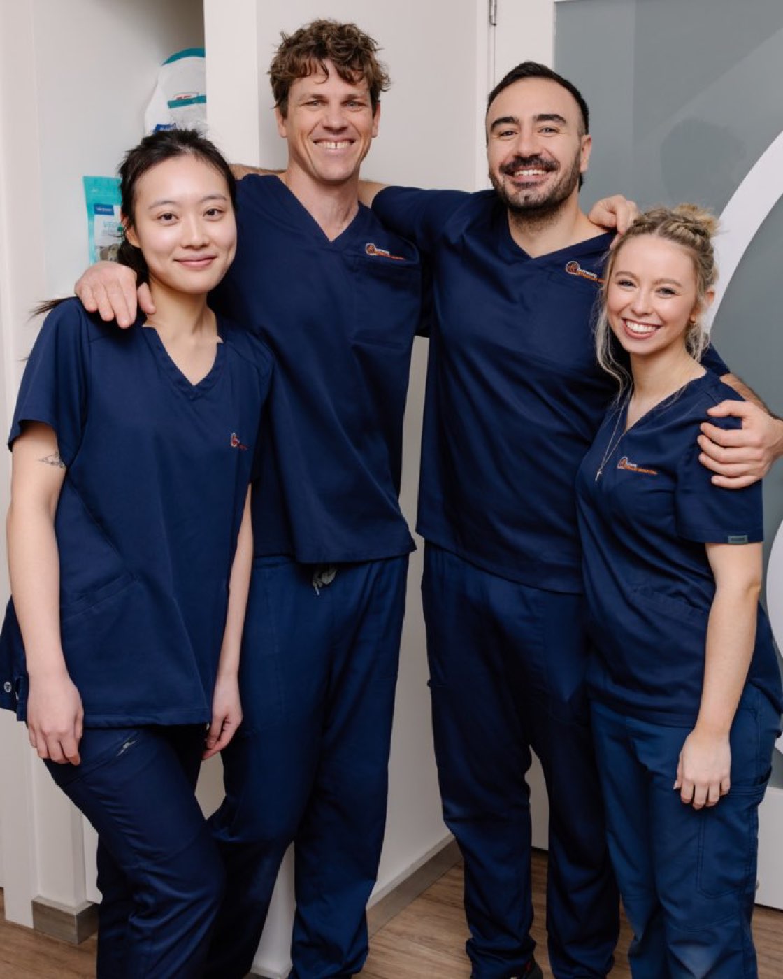 Four members of the Eastwood Veterinary Hospital team in navy hospital scrubs, standing together with their arms around each other